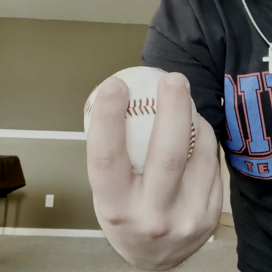 Austin holding a baseball with index and middle fingertips crossing the wide horseshoe seam.